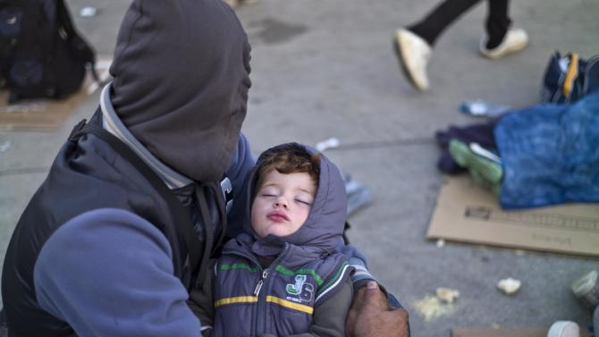 A Syrian refugee man holding his sleeping son, rests on the ground after spending the night at a collection point in the truck parking lot of the former border station on the Austrian side of the Hungarian-Austrian border near Nickelsdorf, Austria, Wednesday, Sept. 23, 2015. European Union ministers agreed Tuesday to relocate 120,000 migrants in a move intended to ease the strain on nations Greece and Italy which are on the frontline of the continent’s overwhelming migrant crisis. (AP Photo/Muhammed Muheisen)
