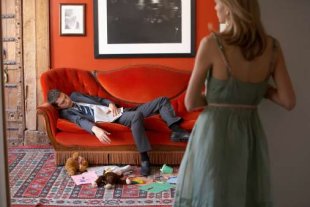 Man on sofa surrounded by mess, woman standing in background