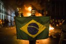 In this photo taken Monday, June 17, 2013, a demonstrator holds a Brazilian flag in front of a burning barricade during a protest in Rio de Janeiro in Rio de Janeiro, Brazil. President Dilma Rousseff has tried to placate the largely middle-class crowds by supporting their right to protest, and the Sao Paulo municipal government has rescinded the 10-cent hike in bus and subway fares that sparked the demonstrations in the first place. But as the protests grow even bigger, with two major marches called for Thursday, the Brazilian government seems at a loss over how to address the sweeping, urgent demands of its people. (AP Photo/Felipe Dana)