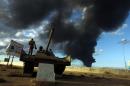 A member of the Libyan army stands on a tank as heavy black smoke rises from the port in the background after a fire broke out at a car tyre disposal plant during clashes against Islamist gunmen in Benghazi on December 23, 2014