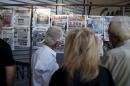 People read newspapers hanging outside a kiosk in Omonia Square in central Athens