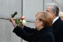 German Chancellor Angela Merkel (L) and Berlin Mayor Klaus Wowereit (R) put roses in a preserved segment of the Berlin Wall during the commemorations to mark the 25th anniversary of its fall on November 9, 2014