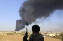 A fighter from Zintan brigade watches as smoke rises after rockets fired by one of Libya's militias struck and ignited a fuel tank in Tripoli