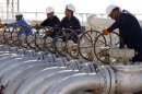 Workers adjust the valves of oil pipes at West Qurna oilfield in Iraq's southern province of Basra