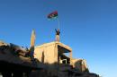 Fighter of Libyan forces waving a Libyan flag flashes victory sign as he stands atop the ruins of a house after forces finished clearing Ghiza Bahriya, the final district of the former Islamic State stronghold of Sirte