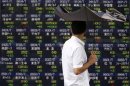 A pedestrian holding an umbrella walks past a stock quotation board displaying various stock prices outside a brokerage in Tokyo