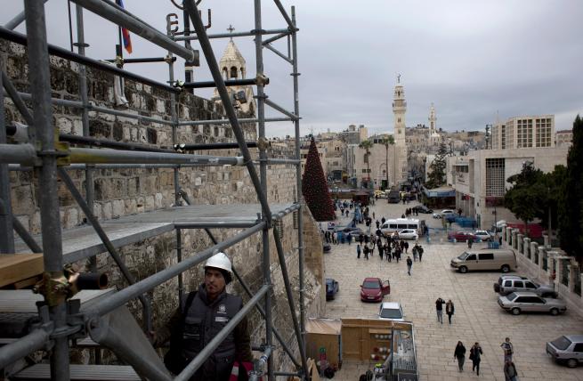 In this Tuesday Dec. 10, 2013 photograph, tourists walk around the Church of the Nativity in the West Bank city of Bethlehem. To visitors arriving in Bethlehem for Christmas this year the Nativity Church will look different. Wrapped in scaffolding, the basilica is having a much-needed facelift after 600 years. Last year it has been included in UNESCO's list of endangered World Heritage sites. (AP Photo/Nasser Nasser)