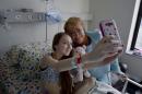 In this photo released by Chile's presidential press office, Chile's President Michelle Bachelet, right, poses for a selfie with Valentina Maureira, who suffered of cystic fibrosis at a hospital in Santiago, Chile, Saturday, Feb. 28, 2015. Maureira post a video in the web asking a meeting with Bachellet to allow her "sleep for ever". (AP Photo/Chile's presidential press office)