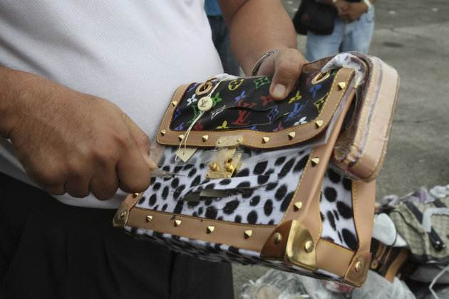 A Government worker uses a cutter to slash a counterfeit Louis Vuitton handbag during a ceremonial destruction of counterfeit goods seized in raids recently at parade grounds of the Philippine National Police at suburban Quezon city, northeast of Manila, Thursday June 30, 2011. The ceremonial destruction of pirated DVDs and other counterfeit goods was done to coincide with the global celebration and awareness campaign known as World Anti-Counterfeiting Day. (AP Photo/Bullit Marquez)