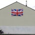 People walk past a house displaying a Union flag in the Shankill Road area of West Belfast