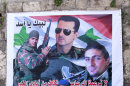 In this Tuesday, April. 30, 2013 photo, a Lebanese man passes in front of a large poster of Syrian President Bashar Assad, center, and two Alawite fighters killed in Syria with Arabic writing that reads, "at your service, oh Assad," and, "bullets will not terrify us and we are not scared of traitors," in the predominantly Alawite neighborhood of Jabal Mohsen in the northern port city of Tripoli, Lebanon. Lebanese members of the Syrian leader's Alawite sect fear their tiny community will be a casualty of the civil war raging in the neighboring country. Already, Sunni extremists have stoned a school bus, vandalized stores and beaten or stabbed a number of men in a wave of attacks against Lebanese Alawites, raising fears of more violence should Assad be removed from power. (AP Photo/Bilal Hussein)