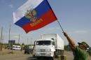 A local resident holds a Russian national flag as lorries, part of a Russian humanitarian convoy cross the Ukrainian border at the Izvarino custom control checkpoint, on August 22, 2014