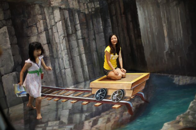 Woman poses for a photograph in front of 3D painting at 2012 Magic Art Special Exhibition in Hangzhou