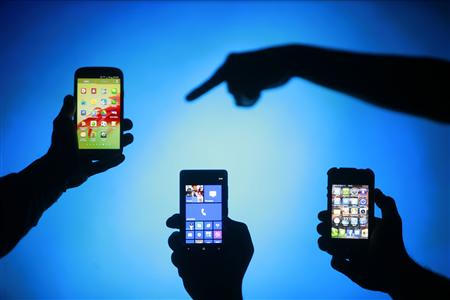Men are silhouetted against a video screen as they pose with Samsung Galaxy S3, Nokia Lumia 820 and iPhone 4 smartphones (L-R) in this photo illustration taken in the central Bosnian town of Zenica, in this May 17, 2013 file photo. REUTERS/Dado Ruvic/Files