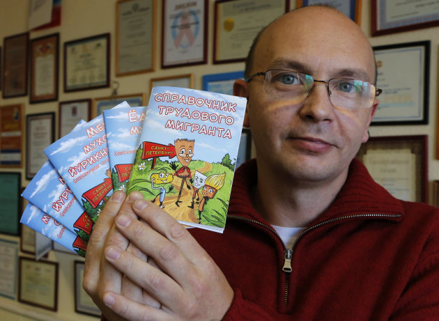 In this photo made Monday, Oct. 22, 2012, Gleb Panfilov, deputy head of the Look into the Future group that published A Labor Migrant's Handbook, shows covers of the book in the Russian, Uzbek, Kyrgyz and Tajik languages in St. Petersburg, Russia. The brochure containing practical advice on how to deal with border guards, police and other authorities was illustrated with images in which migrant workers were represented as paint brushes, brooms and other tools. (AP Photo/Dmitry Lovetsky)