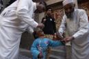 Polio workers give polio vaccine drops to a child as a policeman stands guard during a vaccination campaign in Peshawar