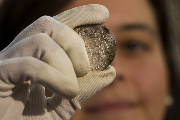 A worker of the ministry holds up for photographers a silver coin from the shipwreck of a 1804 galleon, on its first display to the media at a ministry building, in Madrid, Friday, Nov. 30, 2012. Spanish cultural officials have allowed the first peep at 16 tons (14.5 metric tons) of the shipwreck, 'Nuestra Senora de las Mercedes' a treasure worth an estimated $500 million that a U.S. salvage company gave up after a five-year international ownership dispute. (AP Photo/Daniel Ochoa de Olza)