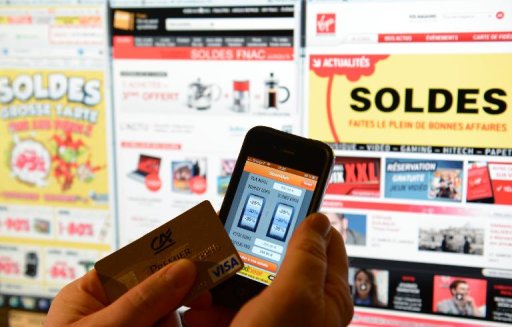 A person holding a credit card and a phone with a sales 'app', in front of websites advertsing for winter sales, on January 9, 2013, in Paris