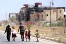 In this Sunday, June 21, 2015 photo, a displaced family walks towards their home in Tikrit, 80 miles (130 kilometers) north of Baghdad, Iraq. Civilians are trickling back into Saddam Hussein's hometown as they look to start anew, the consequences of a year under Islamic State rule conspicuously written on its charred buildings and damaged homes.(AP Photo/ Hadi Mizban)