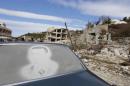 An image of Assad is seen on a car parked in front of damaged buildings in the town of Rabiya